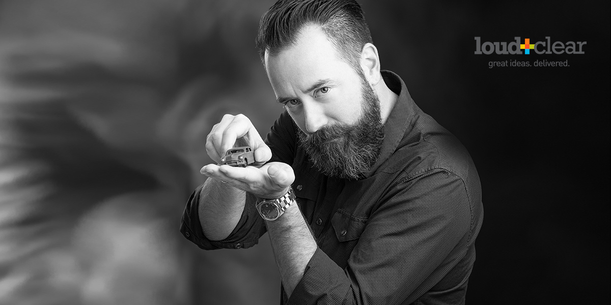 Business Professional posing against mottled gray backdrop holding a toy car for his creative headshot by photographer Brian Yungblut