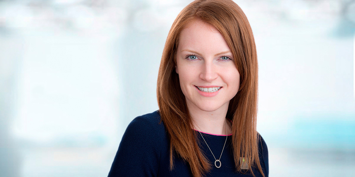 Beautiful red head woman poses on location for company headshot day against a mottled, sky blue custom backdrop